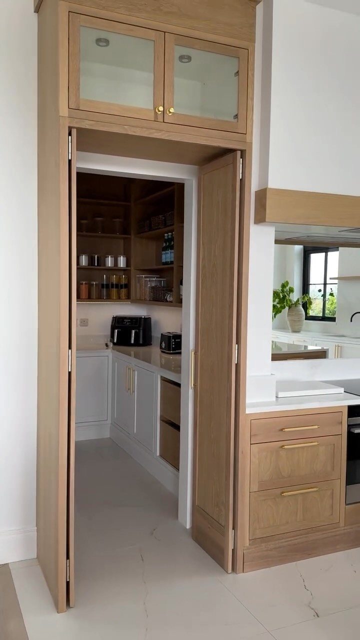 Walk-in pantry with light wood doors and white interior shelving and cabinets.