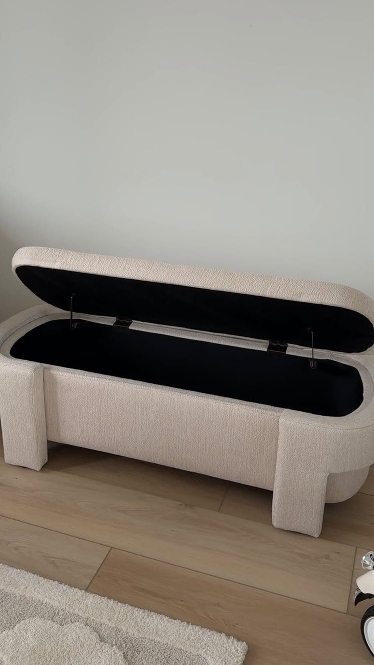Beige fabric storage bench with open lid showing black interior on wood floor