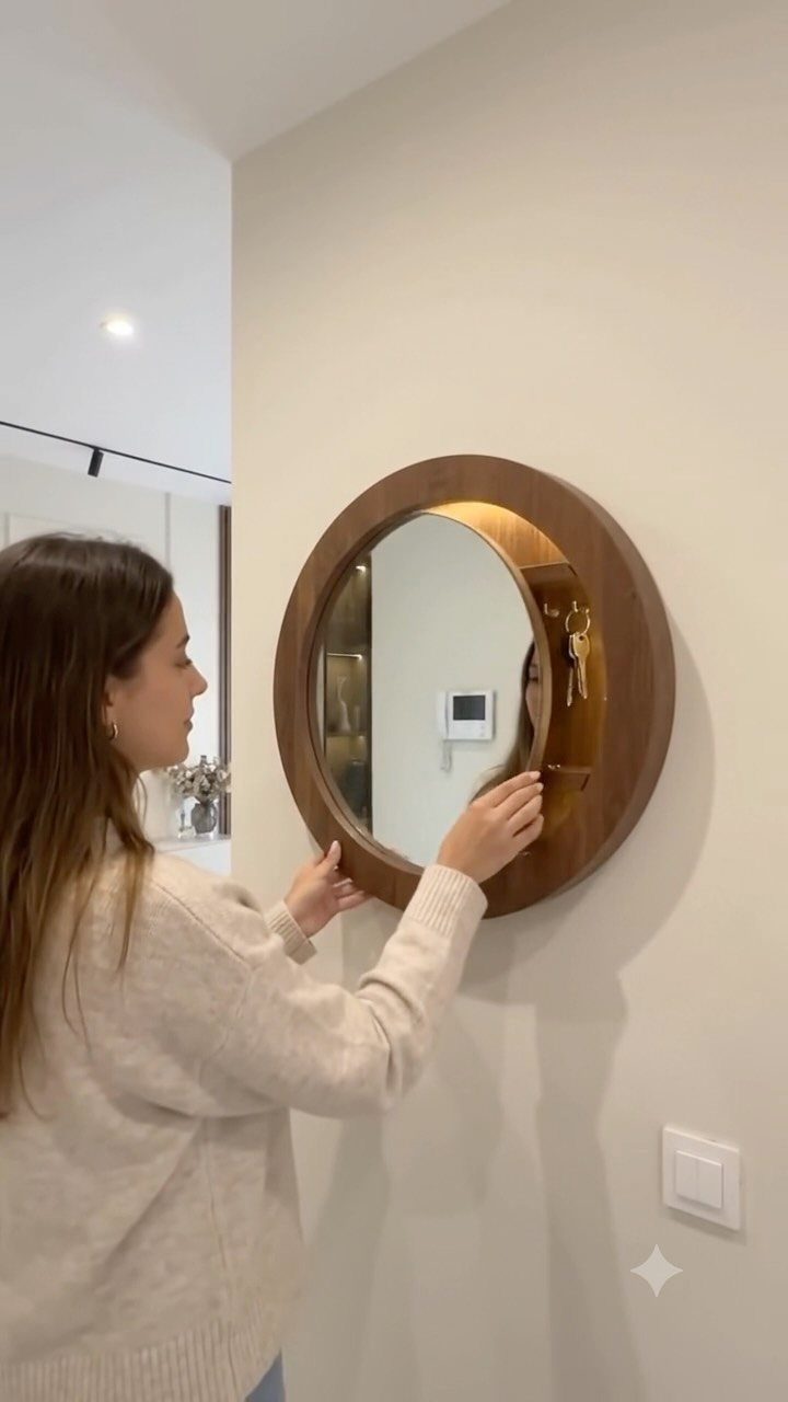 Woman opening a circular wooden wall mirror to reveal hidden storage inside.