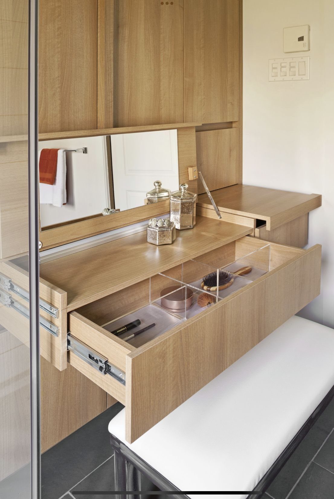 Light-wood hidden vanity with fold-down table, open storage drawer, and integrated wall mirror.