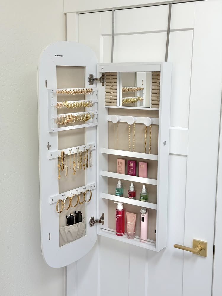 White wall-mounted jewelry cabinet with open oval mirror door and organized accessories.