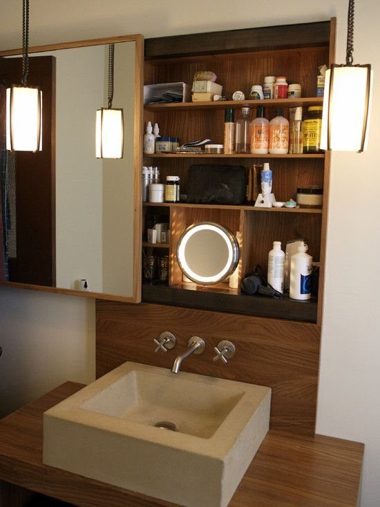 Sliding mirror revealing a wooden storage cabinet with toiletries above a stone bathroom sink.