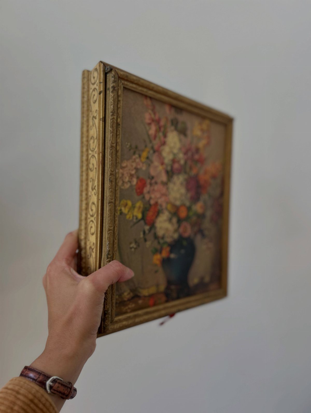 Gold-framed flower painting being opened to reveal a hidden storage compartment behind it