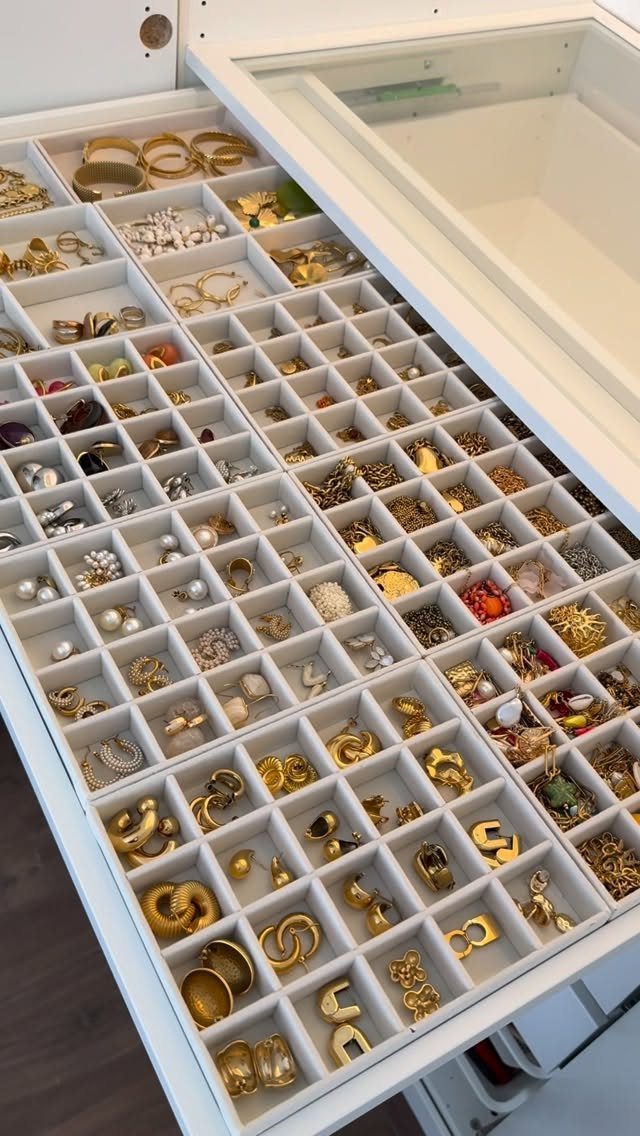 White jewelry organizer drawer with small compartments filled with gold and silver jewelry.