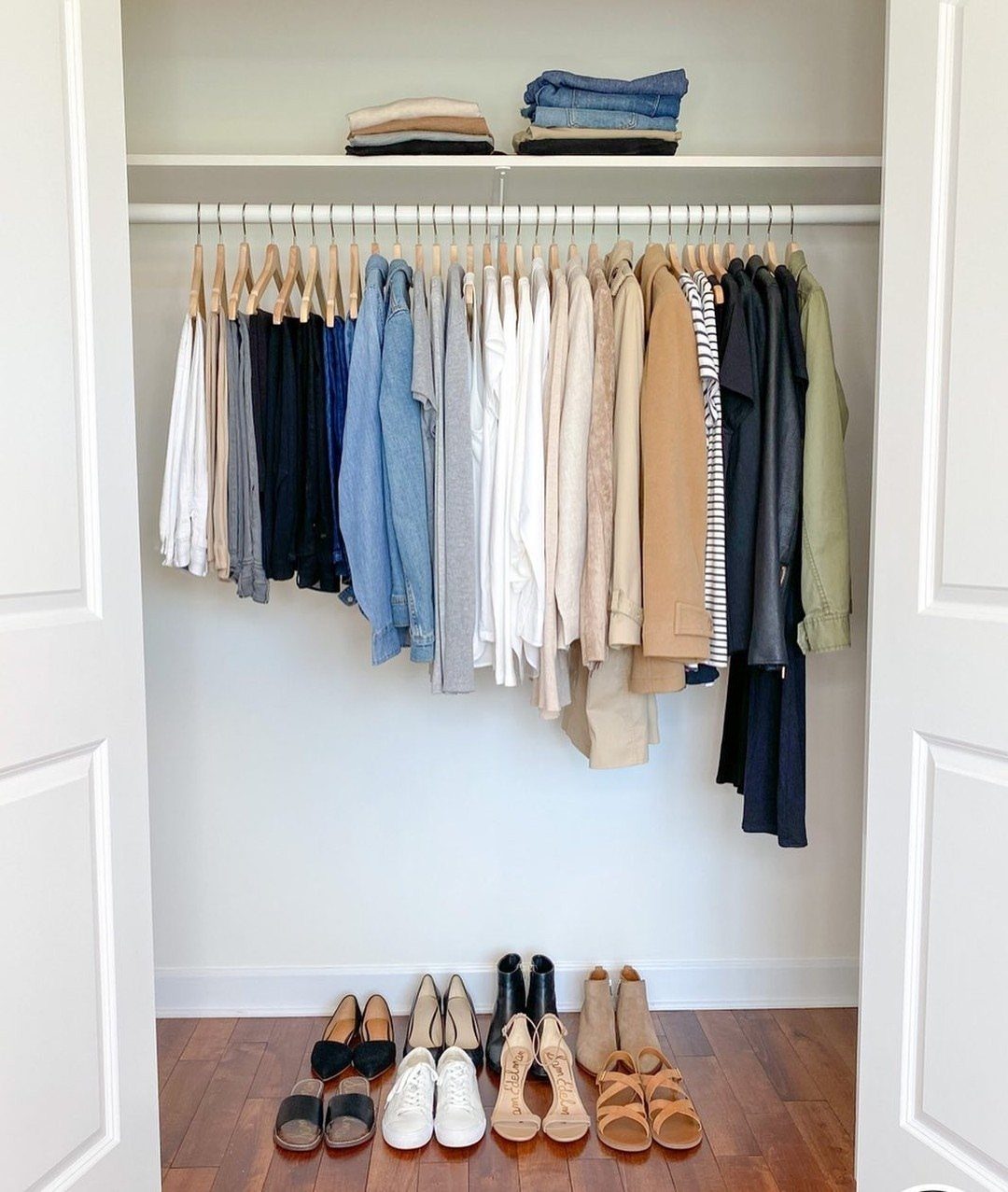 Organized white closet with hanging clothes and shoes arranged on the floor