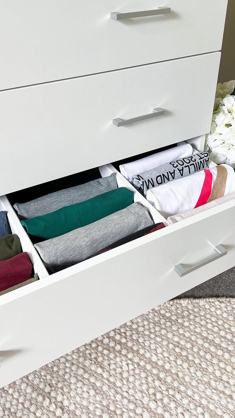 Folded t-shirts in grey, green, and white organized inside a white dresser drawer.