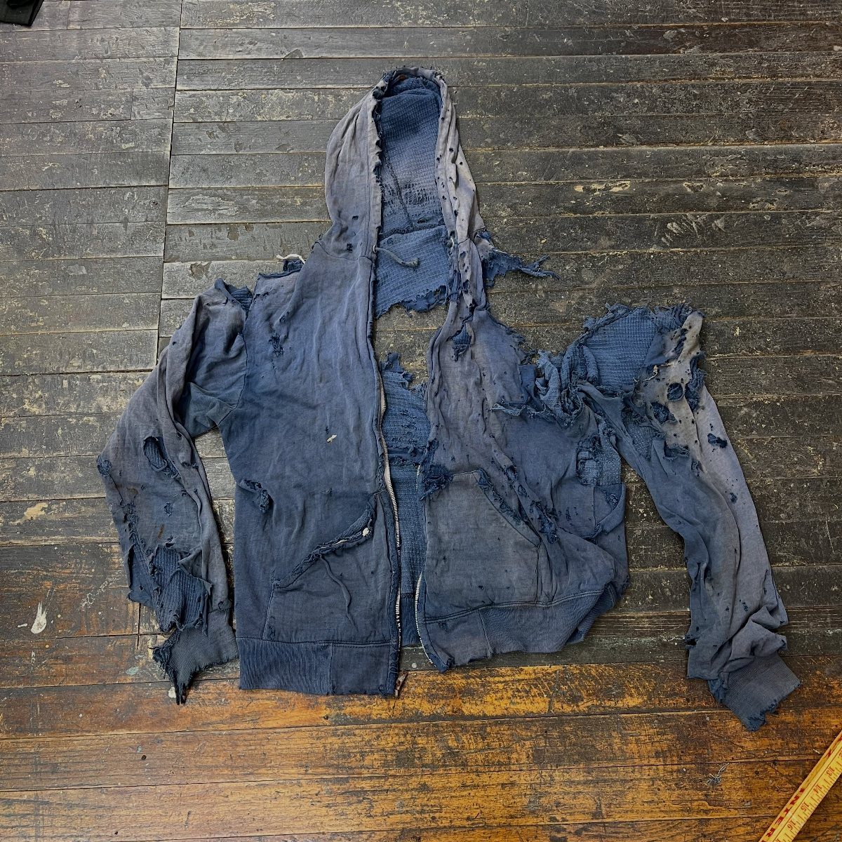 Torn navy blue zip-up hoodie with large holes lying on a wooden floor