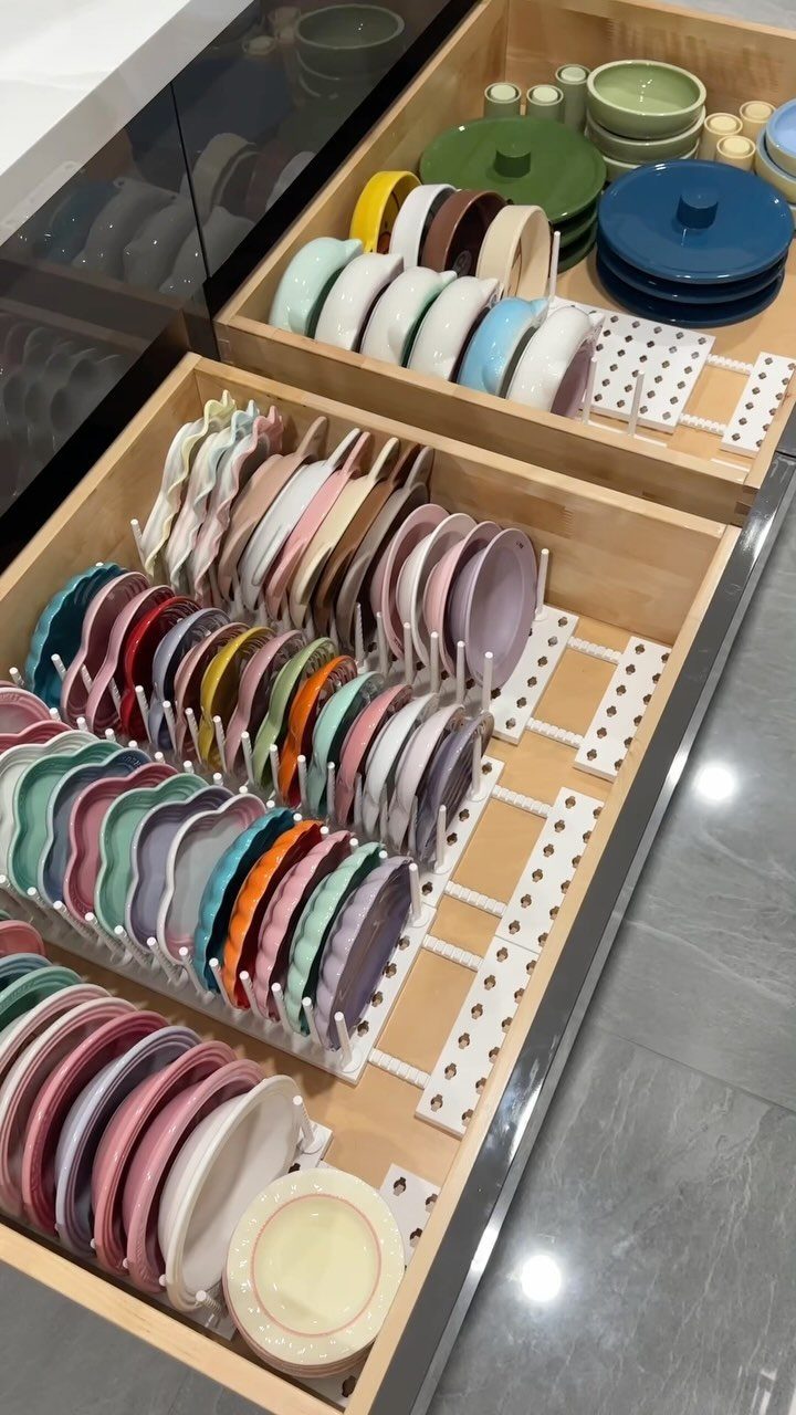 Colorful plates organized by white adjustable peg dividers in a wooden kitchen drawer.