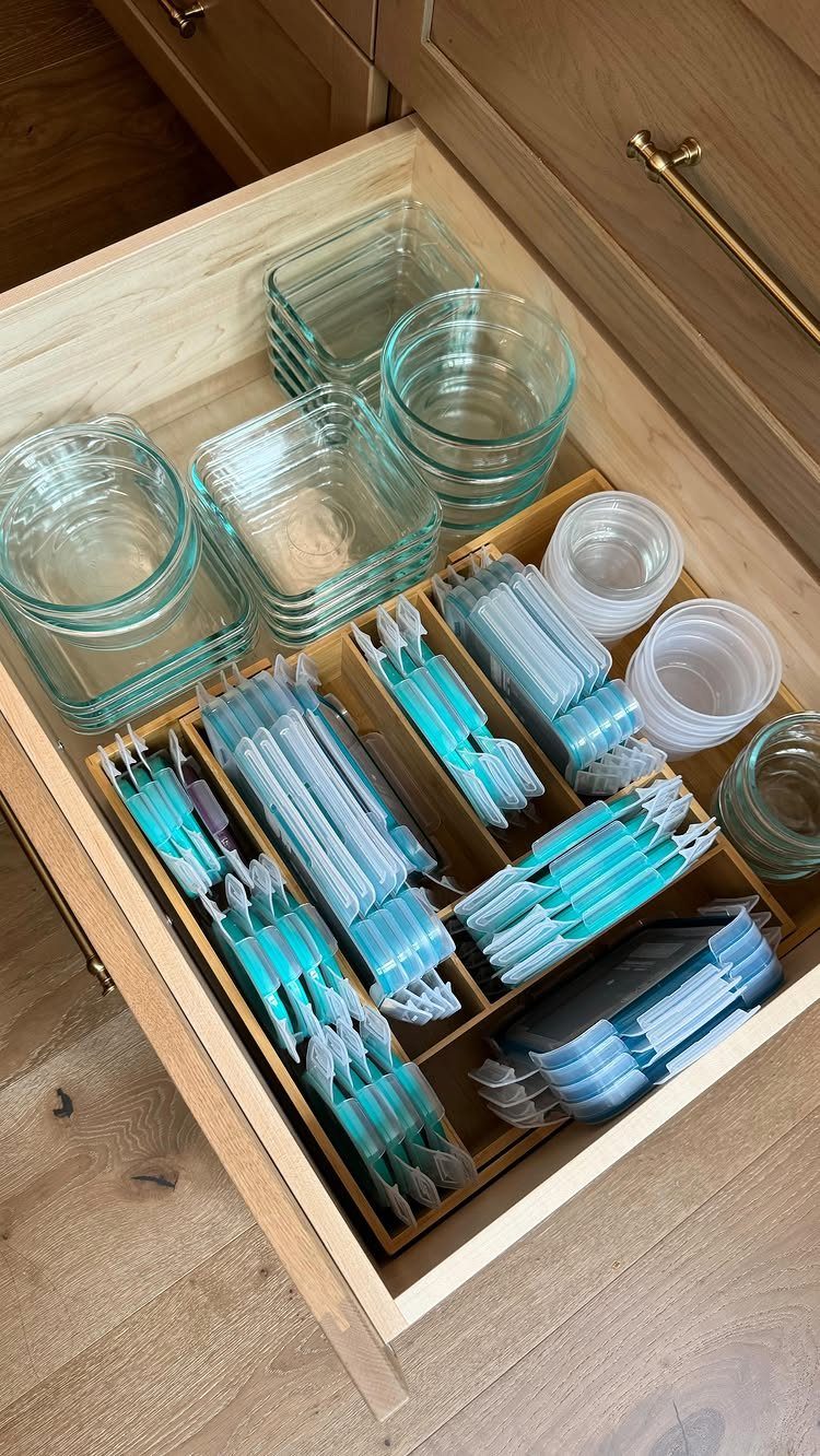 Open light-wood kitchen drawer with glass containers and organized plastic bags in a divider.