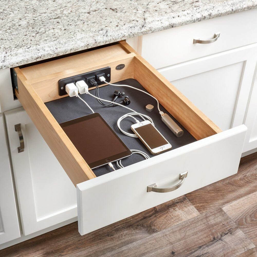 Open white kitchen drawer with power strip charging a tablet and smartphone.