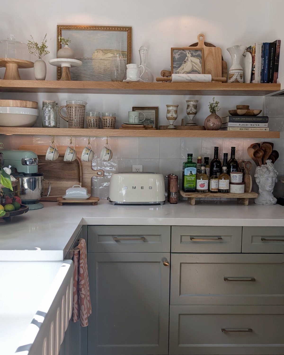 Two light-wood floating shelves holding kitchenware and decor above grey kitchen cabinets.