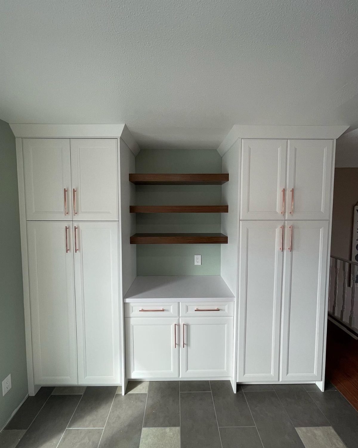 White kitchen cabinets and pantry cupboards with floating wooden shelves and gold handles.