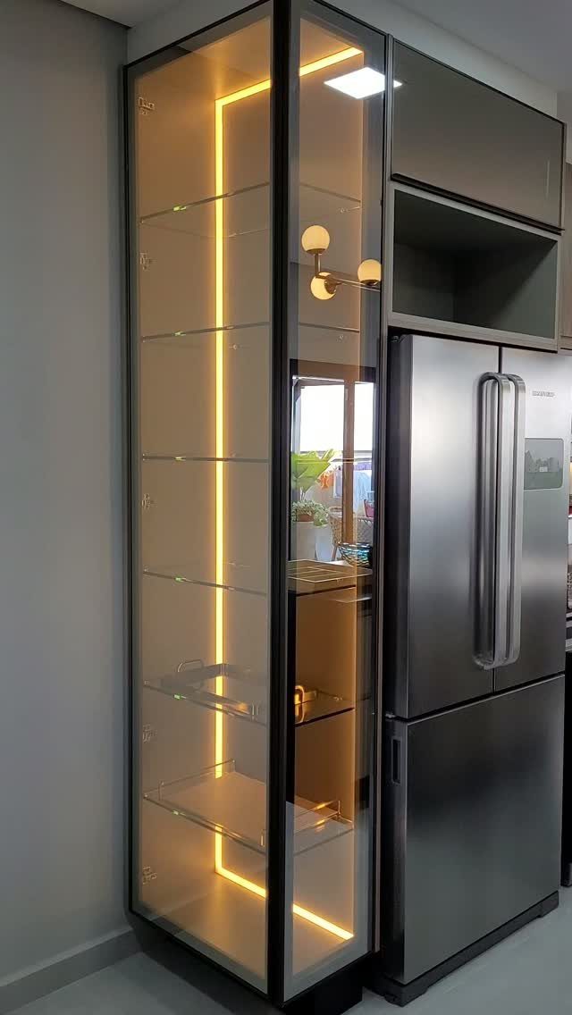 Glass-front kitchen cabinet with interior LED lighting and glass shelves next to a refrigerator.