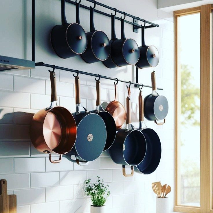 Black and copper pots and pans hanging from black metal rails on white tiles