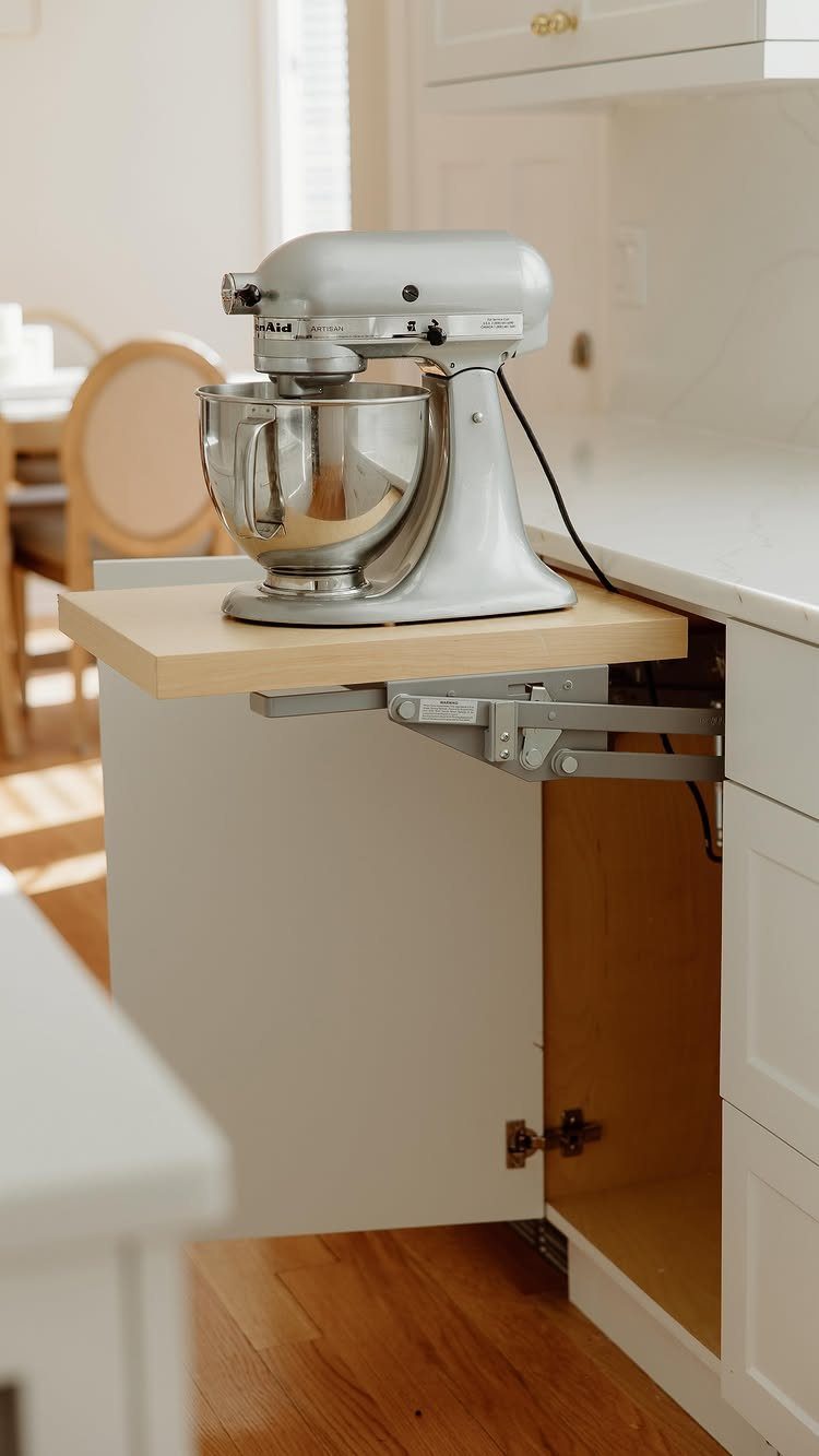 Silver stand mixer on a mechanical lift platform emerging from a white cabinet.
