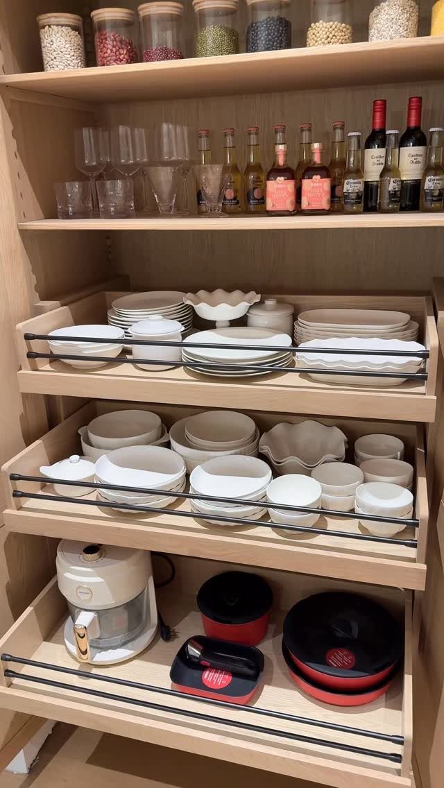 Wooden kitchen cabinet with multiple pull-out shelves holding white ceramic dishes and cookware.