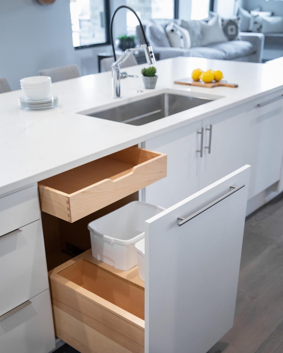 White kitchen island cabinet open to reveal a pull-out trash bin and drawer.