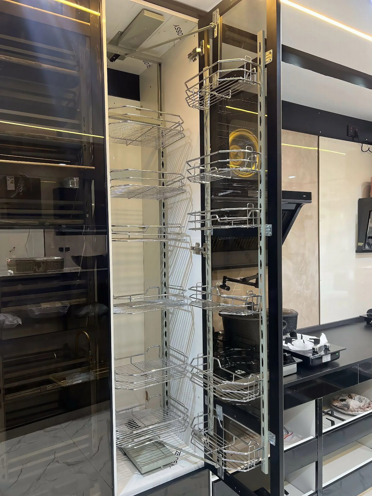 Slim pull-out pantry with chrome wire baskets in a modern dark kitchen.