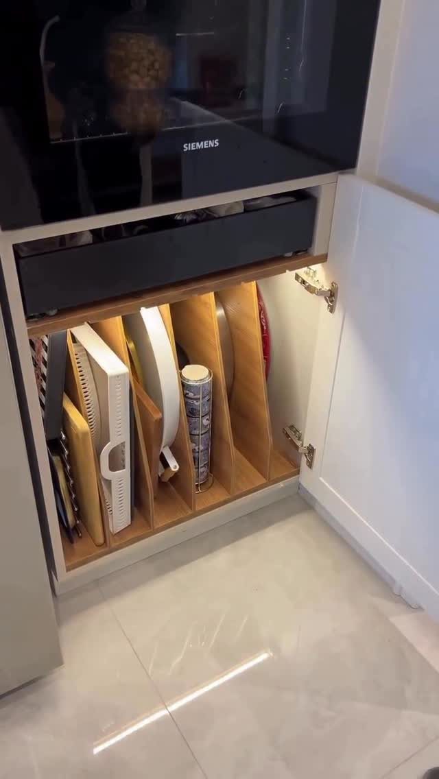 Wooden vertical dividers in a white kitchen cabinet storing platters and containers upright.