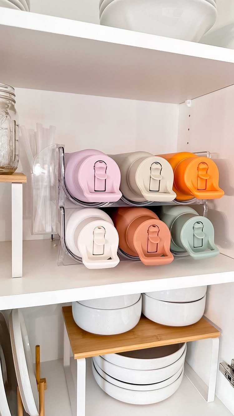 Two-tier acrylic rack holding colorful reusable water bottles horizontally on a white shelf.