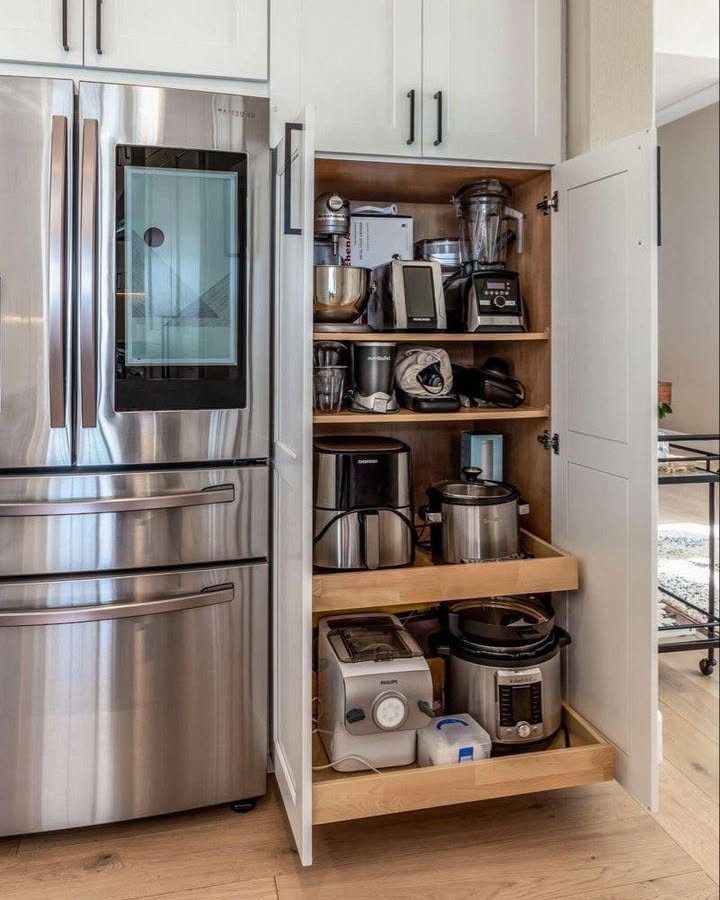 White kitchen cabinet with open doors storing various small kitchen appliances on shelves.