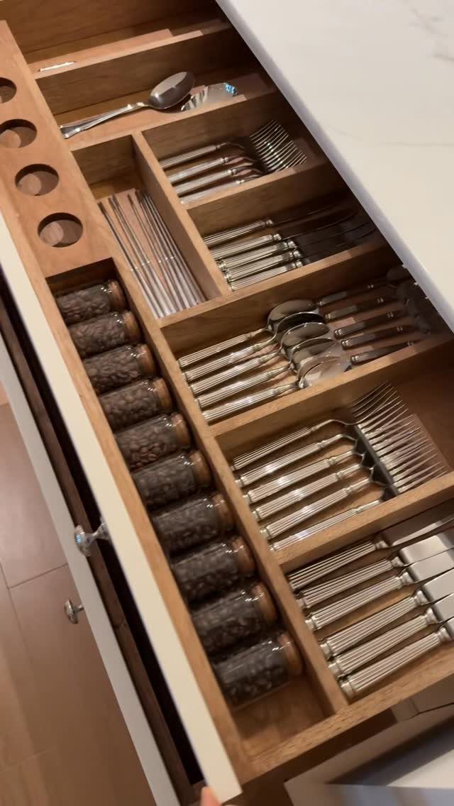 Open kitchen drawer with wooden dividers organizing silverware and small spice jars.