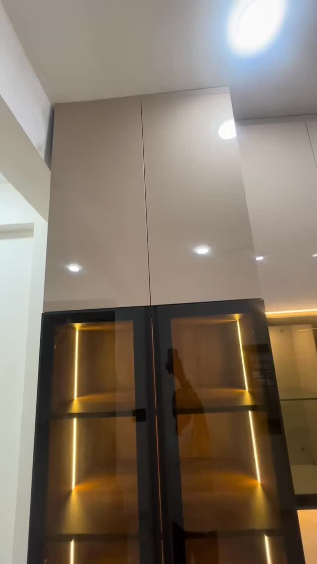 Modern kitchen cabinet with glass doors and warm vertical interior LED strip lighting.