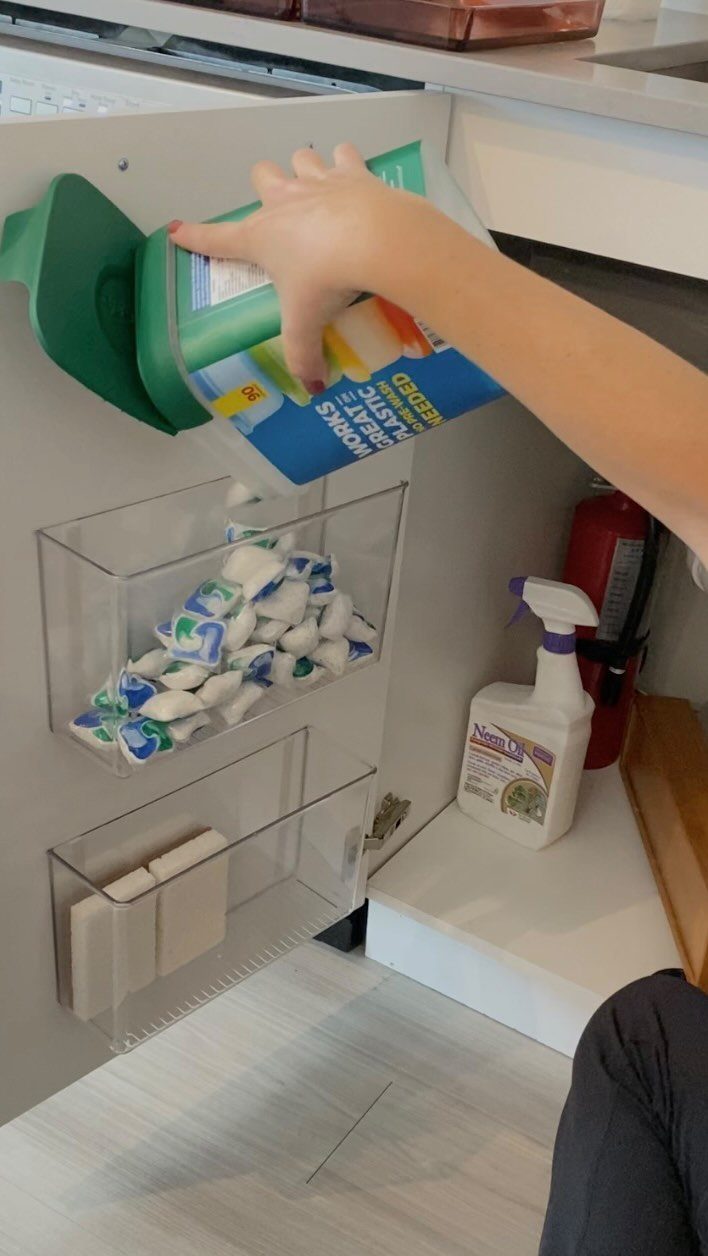 Clear acrylic bins attached to the inside of a white cabinet door holding supplies.