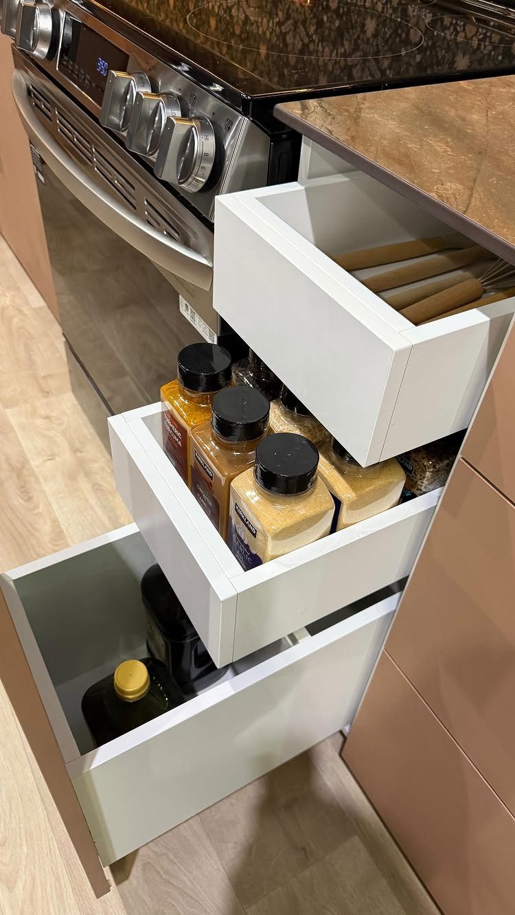 White pull-out kitchen cabinet drawers containing various spice jars and bottles of oil.