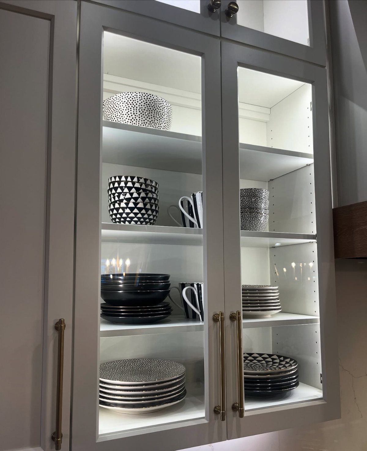 White glass-front kitchen cabinets with interior lighting displaying black and white dinnerware.