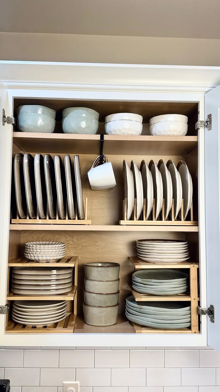 Open white kitchen cabinet with organized ceramic plates and bowls on wooden shelves.