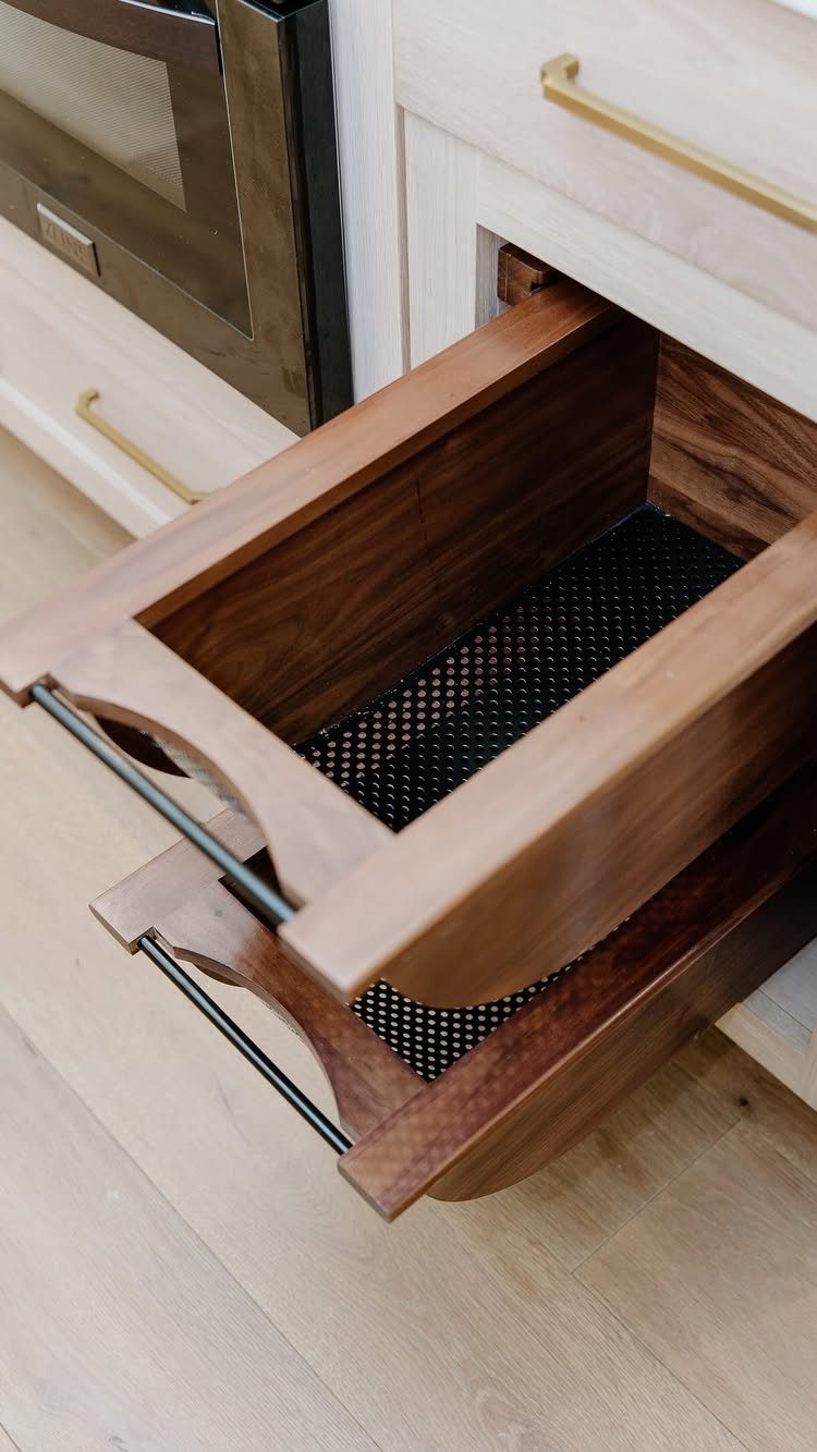 Wooden pull-out cabinet drawers with black liners and dark metal handles in a kitchen.