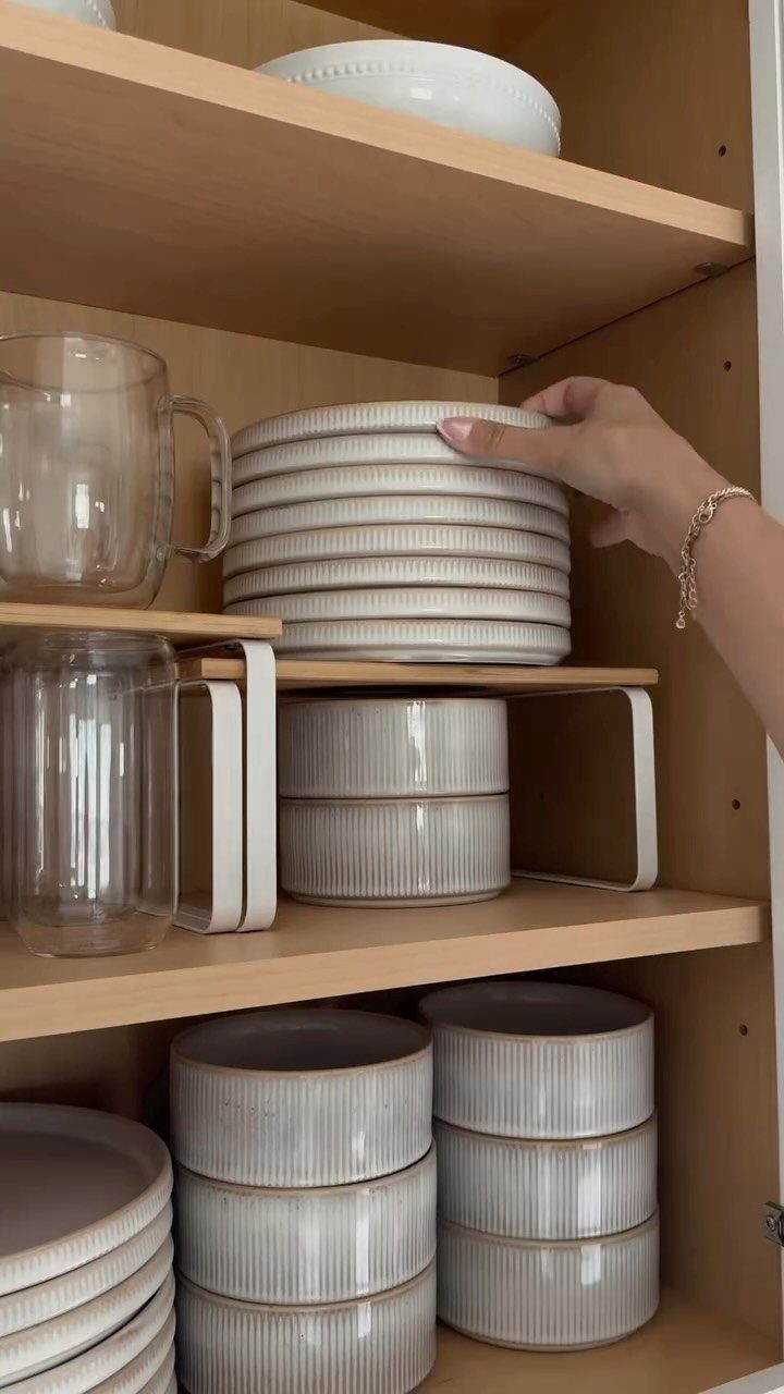 White metal shelf riser holding a stack of plates inside a wooden cabinet.