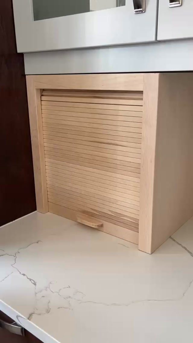 Tambour slatted sliding door on a light wood kitchen cabinet above white marble countertop