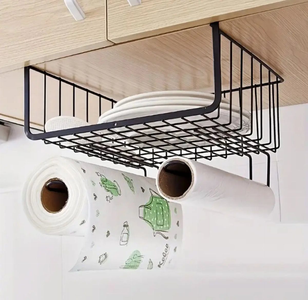 Black wire under-shelf basket holding white plates attached to a light wood cabinet.