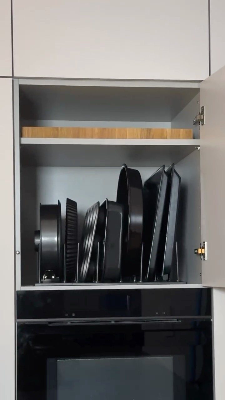 Black baking sheets stored upright in a vertical organizer inside a grey cabinet.
