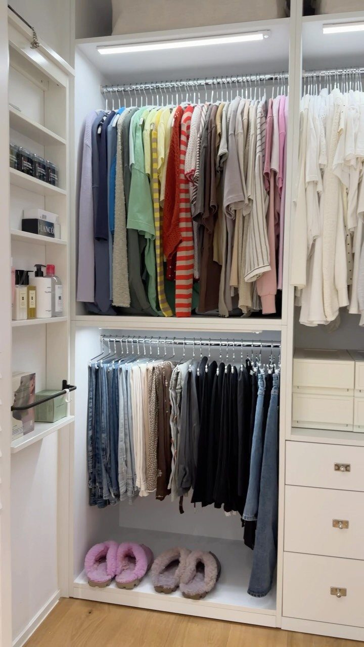 Organized white closet with tops grouped by color and sleeve length on rods.