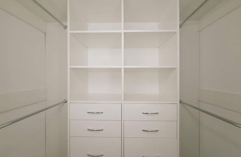 White built-in closet organizer with open shelves, drawers, and side hanging rods.