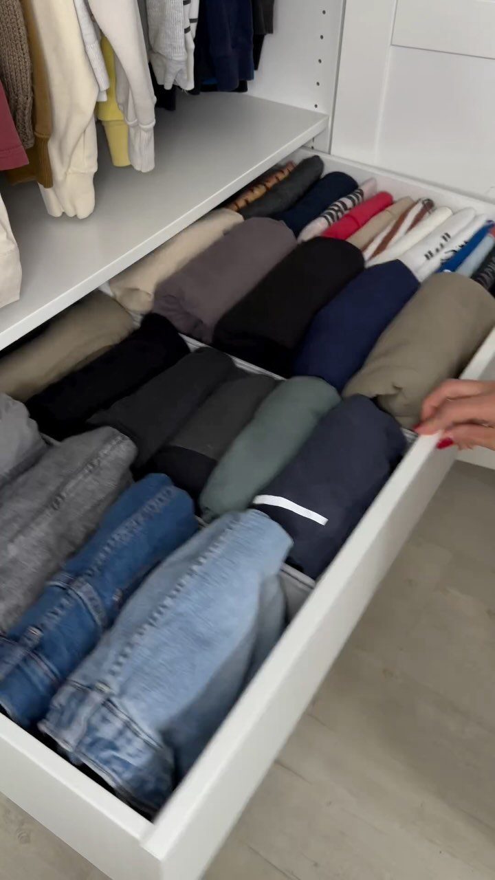 Folded t-shirts and jeans arranged vertically in a white closet drawer.