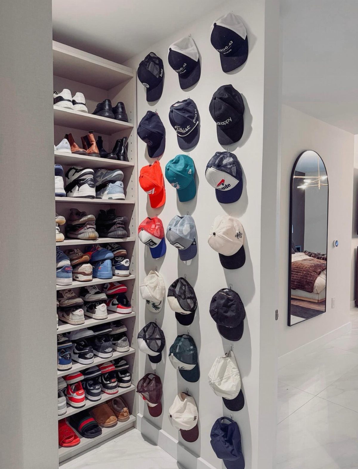 Baseball caps mounted on a white wall next to a shoe shelving unit.