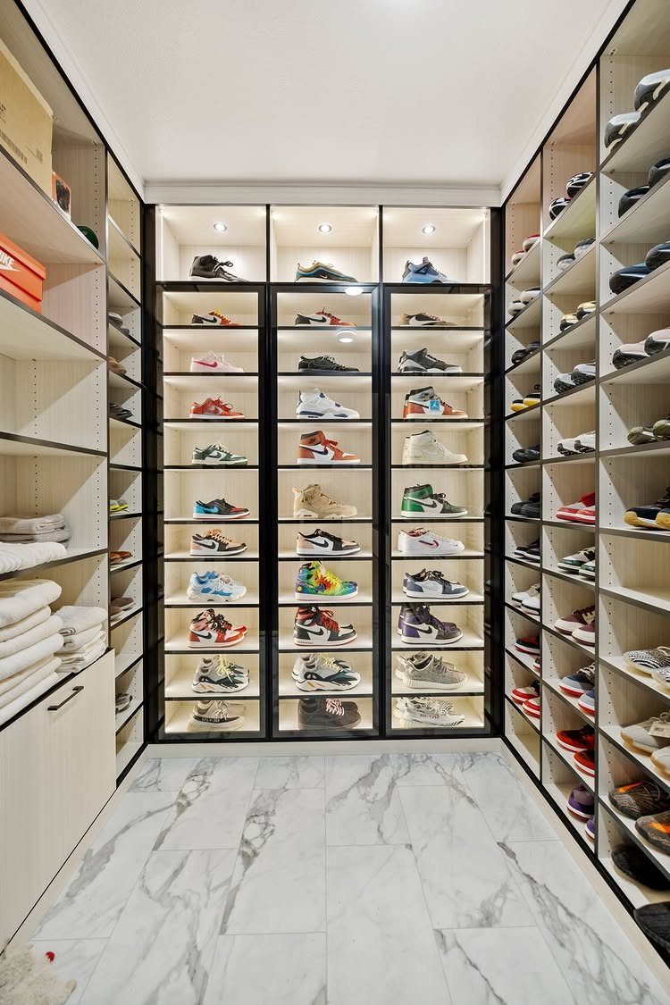 Sneakers organized on open white shelving and glass display cases in a marble closet.