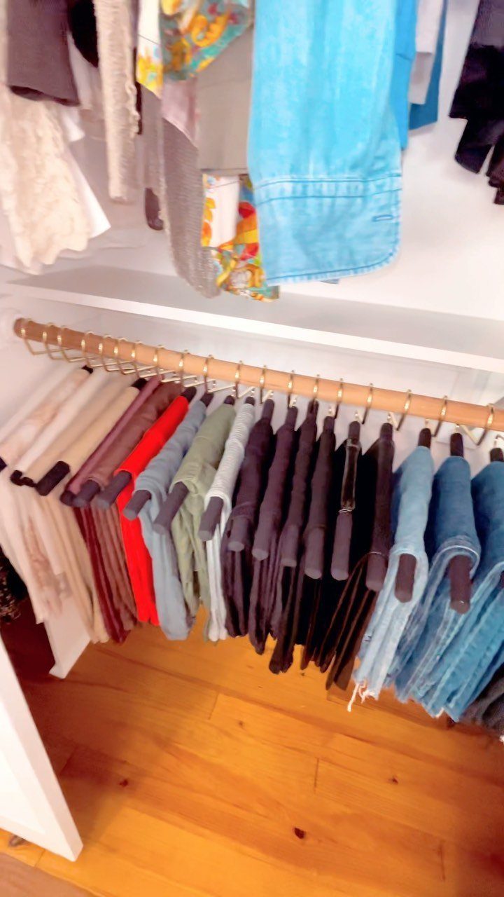 Pants in various colors hanging on slim black velvet hangers on a gold rod.