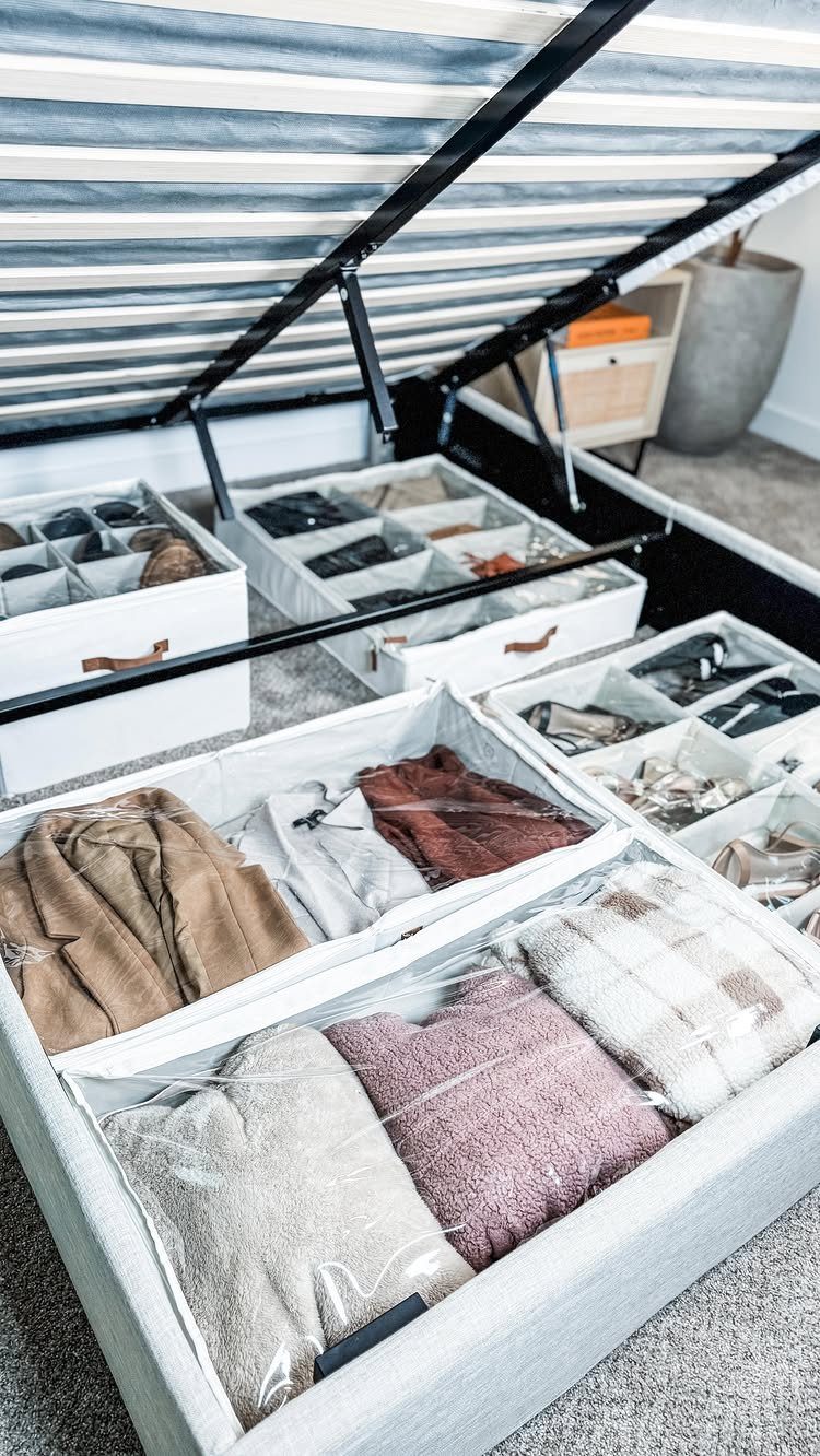 Lift-up storage bed containing white fabric bins with folded clothes and accessories.