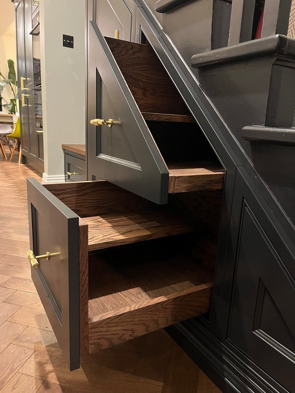 Dark grey under-stairs storage drawers with natural wood interiors and gold handles.