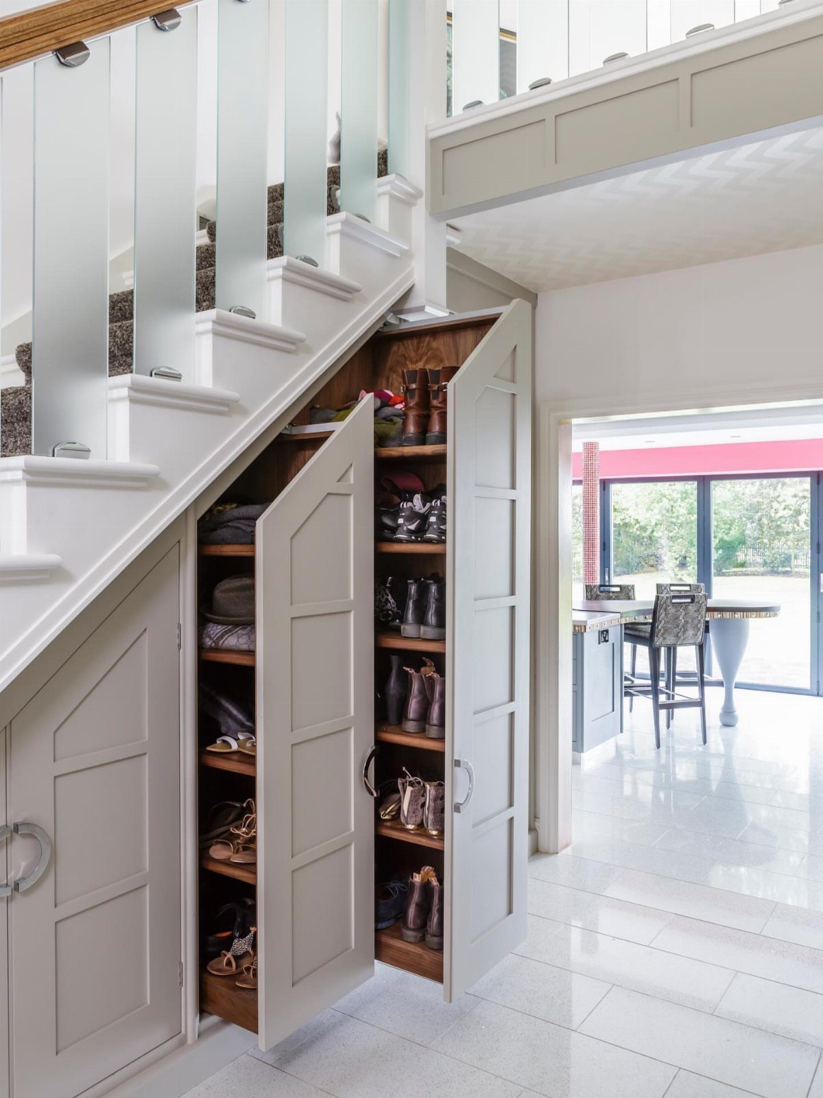Built-in under-stairs closet with open doors showing shelves of boots and shoes.