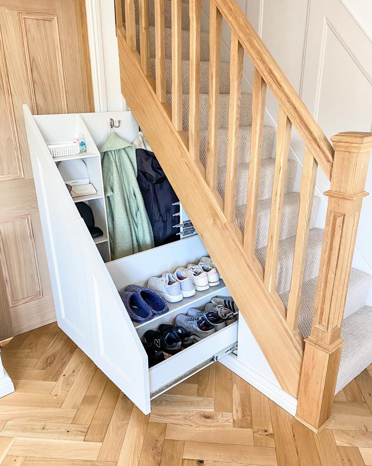 White under-stairs mudroom closet with hanging coats and a pull-out shoe drawer.