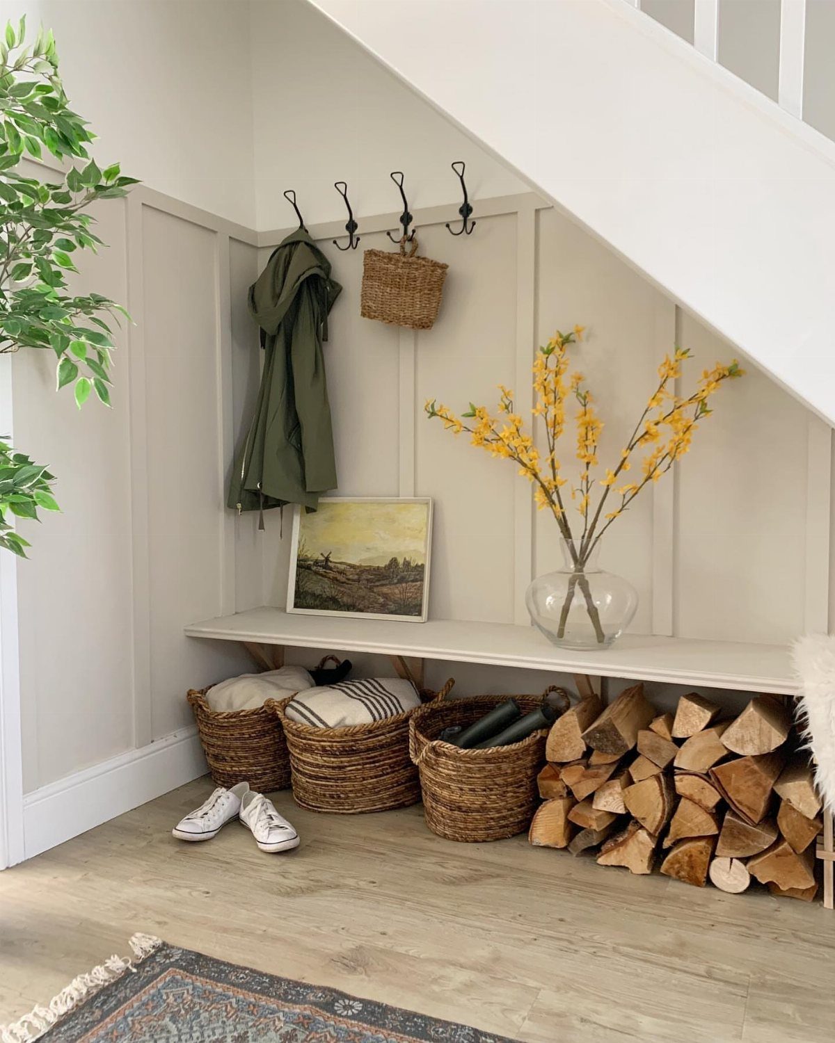 Mudroom under stairs with a white bench, woven baskets, and stacked firewood.