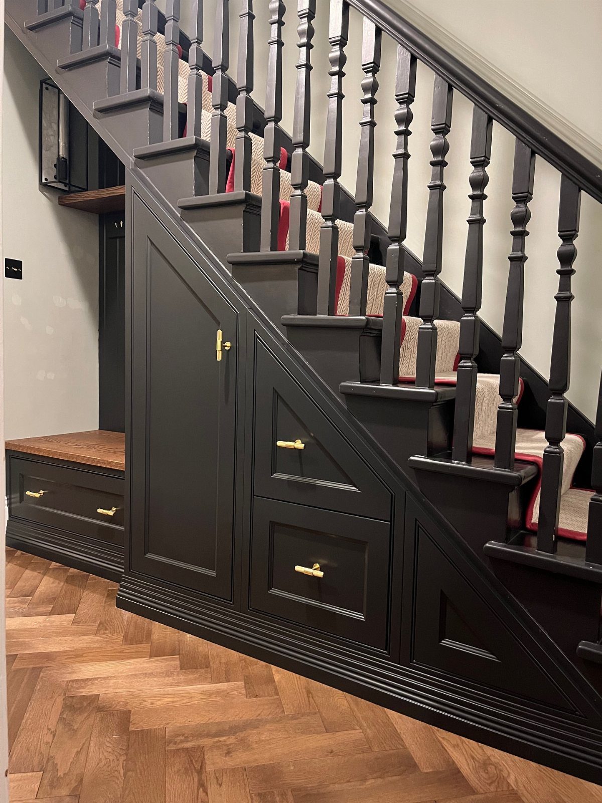 Dark grey under stairs closet with gold hardware and herringbone wood flooring.