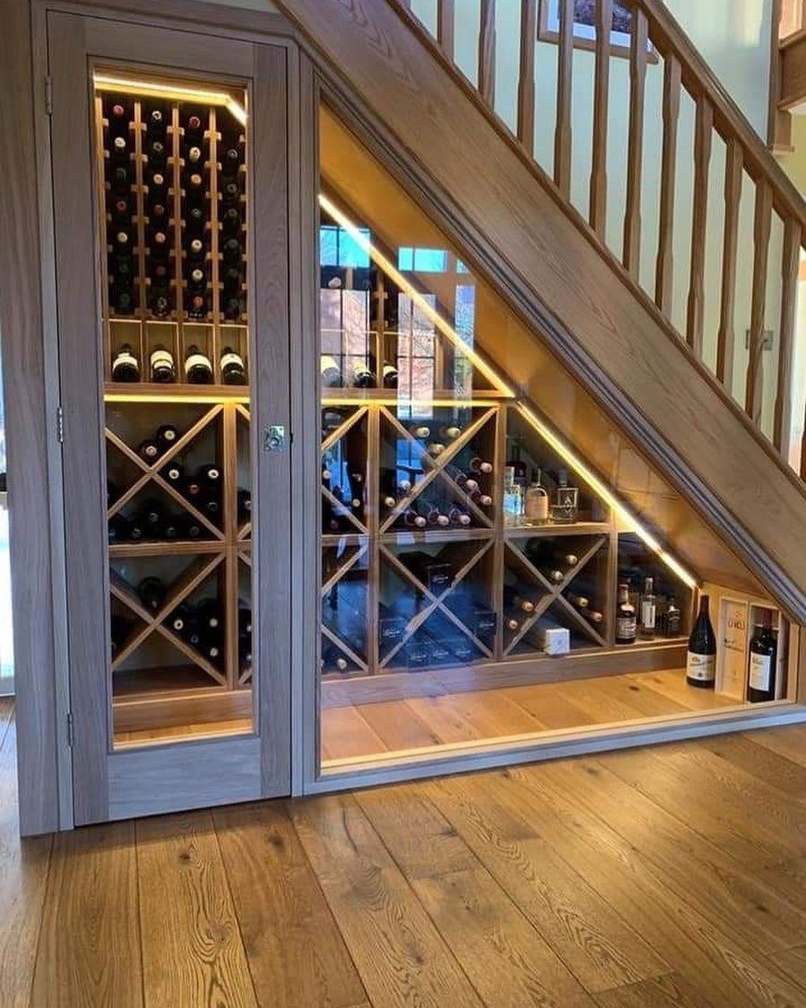 Built-in wine rack with glass doors and lighting installed under a wooden staircase.