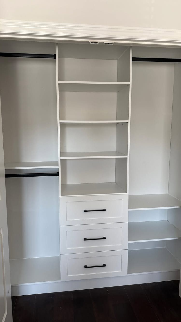 White built-in closet organizer with shelves, drawers, and hanging rods in a narrow space.